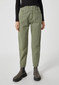 Pantalones de algodón verdes con un ajuste relajado, que cuentan con una cintura fruncida, dos bolsillos delanteros y se combinan con botas chunky marrón oscuro.