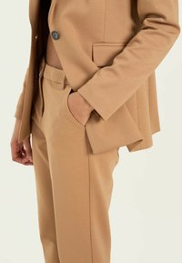 Beige räätälöity bleiseri napilla ja sivutaskulla, yhdistettynä samansävyisiin housuihin, joissa on sileä pinta ja siistit linjat.