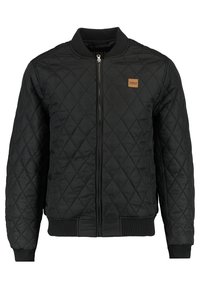 Black quilted bomber jacket with ribbed collar, cuffs, waistband, front zipper, and small brown logo patch on the left chest.
