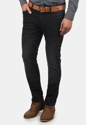 Schwarze DenimJeans mit Slim-Fit, ausgestattet mit einem klassischen Fünf-Taschen-Design und einem braunen Ledergürtel. Getragen mit braunen Stiefeletten.