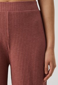 Rippenstoff in Rosa für Leggings mit einem hohen Bund, der vertikale Muster und eine weiche Textur zeigt, betont durch die Handplatzierung nahe der Naht.