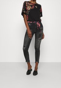 Svart blommig topp med lös passform, kombinerad med slitna svarta slim-fit jeans med fransar och glänsande detaljer. Svarta mules.