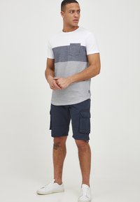 Klassisk T-skjorte med rund hals i bomull, hvit med marineblå striper; kombinert med marineblå cargo-shorts og hvite joggesko. Har en brystlomme.