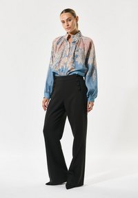 Vloeiende blouse met bloemenpatroon in lichtblauw en roze, met een hoge hals en knoopdetails. Zwarte high-waisted broek met zijknopen.