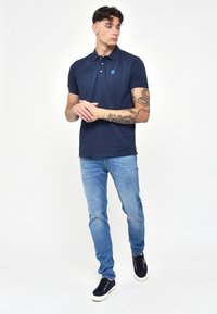 Námořnická modrá polo tričko s krátkým rukávem, límečkem a malým logem. V kombinaci s světle modrými džínami a námořnickými teniskami.