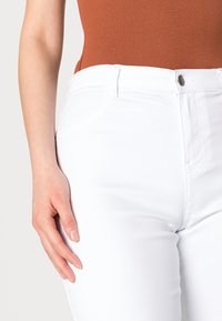 Witte denim jeans met een aansluitend ontwerp, met voorkruiszakken en een knoopsluiting. Glad textuur met zichtbare stikseldetails.