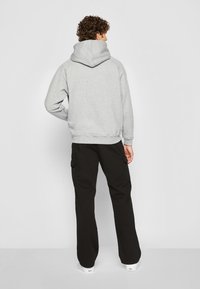 Sudadera gris con capucha y bolsillo tipo canguro, combinada con pantalones cargo negros que tienen bolsillos laterales. Sneakers blancos.