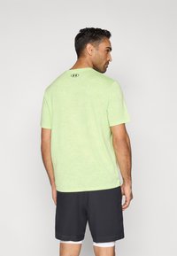 Ανοιχτοπράσινο αθλητικό πουκάμισο με κοντά μανίκια, υφασμάτινη υφή και μικρό λογότυπο στο πίσω μέρος. Συνδυασμένο με σκούρο σορτς.