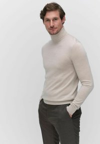 Lichtbeige coltrui gemaakt van zacht materiaal, aangesloten ontwerp met lange mouwen, gedragen met donkergrijze op maat gemaakte broek, minimalistische achtergrond.