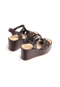 Brown platform sandals with crisscross leather straps, an adjustable ankle strap, and a textured footbed, featuring a rounded wedge sole.