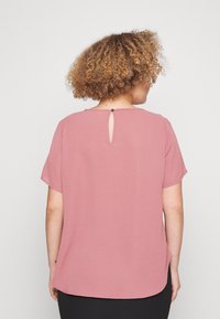 Kortermet, rosa bluse med detalj i nøkkelhullet bak, glatt tekstur og avrundet kant. Mykt stoff med en avslappet passform.