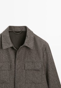 Grå uldfrakke med krave, der har to brystlommer. Stoffet har en tekstureret finish, som fremhæver dets strukturerede design.