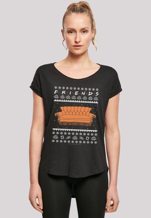 Schwarzes T-Shirt mit kurzen Ärmeln, das ein grafisches Design mit einem orangefarbenen Sofa, dem Wort "FRIENDS" und bunten Akzenten zeigt, vor einem festlichen Hintergrund.