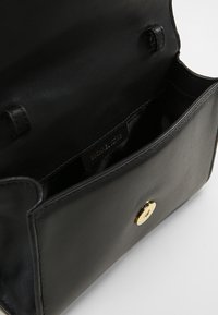 Czarna skórzana torebka z złotymi akcentami. Wnętrze wyłożone materiałem, z pojedynczą komorą i zapięciem na zatrzask. Gładka tekstura na całej powierzchni.