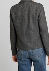 Schwarz-weißer Blazer mit Hahnentrittmuster, taillierte Passform, Kragen und strukturierte Schultern, kombiniert mit hochgeschnittenen Jeans.