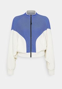 Kort bomberjakke med en øverste sektion i blå striber og en ensfarvet hvid nederste sektion. Har en sort lynlås foran og elastiske manchetter.