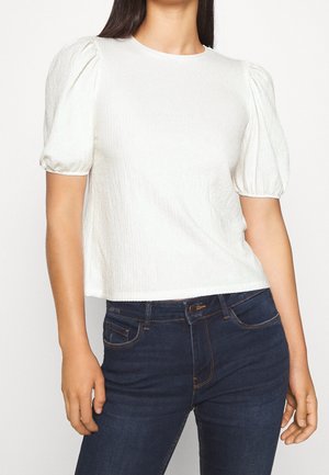 Top bianco a maniche corte con collo rotondo, tessuto testurizzato e maniche a palloncino, abbinato a jeans blu scuro con dettagli cuciti.