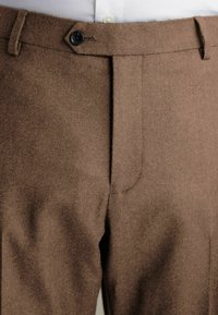 Pantalones de lana marrón con un acabado texturizado, que cuentan con cremallera frontal, cierre de botón único y bolsillos laterales.