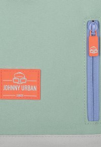 Zöld texturált szövet táska narancssárga címkével, amellyen "JOHNNY URBAN JUNIOR" felirat található, valamint kék cipzárral és narancssárga húzózsinórral.