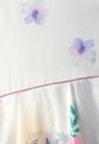 Weißer Stoff mit dezenten Blumenmustern in Pastellfarben. Mit rosa Akzentbesatz entlang der Naht, der eine zarte, strukturierte Optik erzeugt.