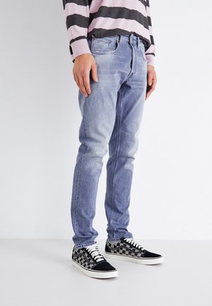 Hellblaue Jeans aus Denim mit einem ausgebleichten Effekt, schmale Passform, Fünf-Taschen-Design, getragen mit schwarz-weißen Schachbrett-Sneakern.