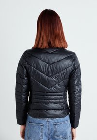 Zwarte pufferjack met een chevron-quiltontwerp, heeft een slim fit en een gladde textuur. De achterkant is eenvoudig zonder zichtbare hardware.