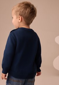 Suéter de punto azul marino con borde y puños acanalados, con cuello redondo y detalle de botones en el hombro, llevado por un niño.