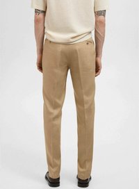 Pantalones beige de corte recto, con bolsillos traseros y una textura sutil. Llevados con una blusa de color claro y mangas cortas.