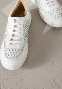 Weiße Sneakers mit einem gewobenen Design, strukturiertem Leder, sechs Ösen und einer glatten Gummisohle. Das Innere verfügt über ein beiges Futter.