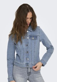 Chaqueta de mezclilla azul con cuello clásico, cierre de botones, bolsillo en el pecho y costuras en el mismo tono. Corte ajustado con mangas largas y ligero deslavado.