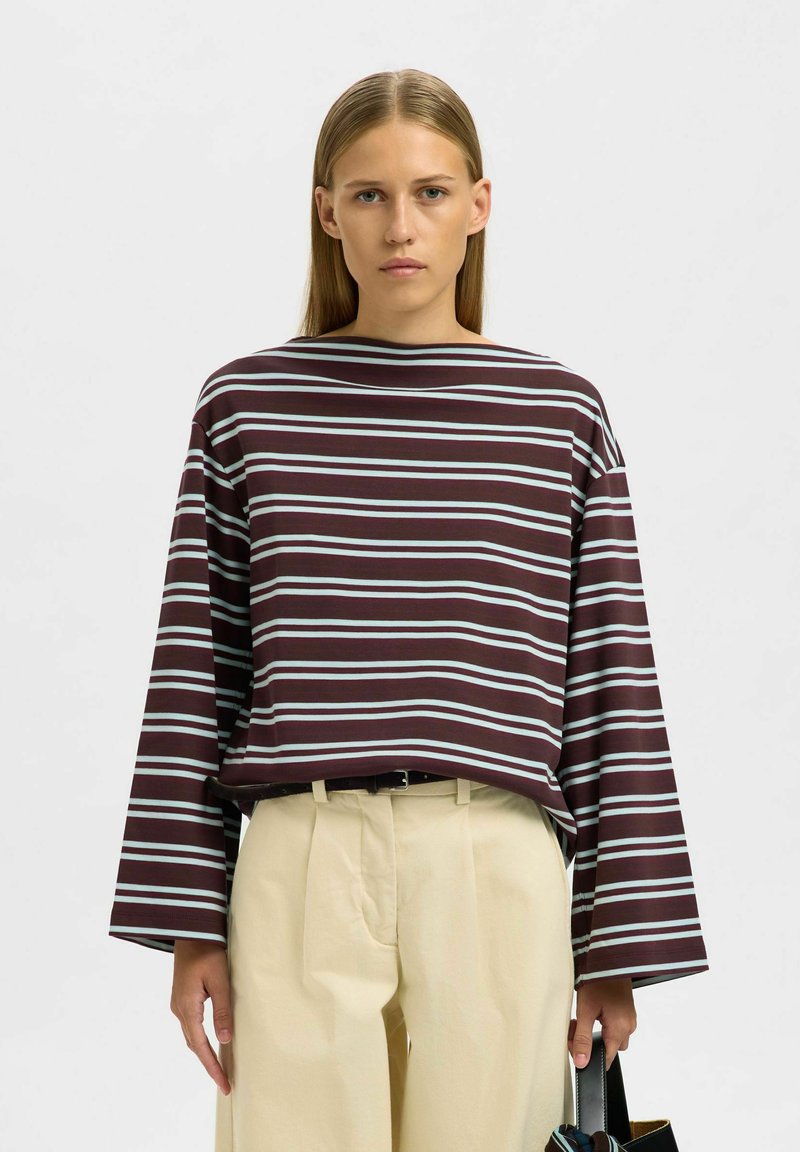 Tumesinine triibuline pluus laiade varrukatega, millel on helesinised horisontaalsed triibud, kombineeritud beežide kõrge vöökohaga pükstega.