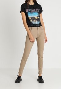 Svart grafisk t-shirt med en färgglad solnedgångsdesign, kombinerad med figurnära beige byxor och svarta snörskor. Släta texturer och avslappnad stil.