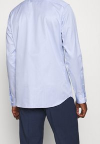 Světle modrá košile s dlouhými rukávy, pruhovaným vzorem, zapínáním na knoflíky na manžetách a zakřiveným lemem, v kombinaci s tmavými kalhotami. Minimalistický design.