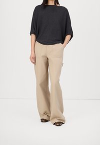 Luźna bluzka w ciemnoszarym kolorze z krótkimi rękawami, zestawiona z beżowymi spodniami o szerokich nogawkach oraz butami w zwierzęcy wzór. Minimalistyczny design i miękka tekstura.