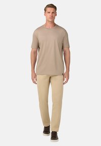 Bežs īsām piedurknēm T-krekls apvienots ar gaiši khaki biksēm. T-kreklam ir apaļa apkakle un gluda tekstūra; bikses ir taisnas. Brūni apavi noslēdz šo izskatu.