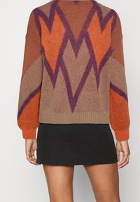 Pull en maille présentant un motif géométrique aux couleurs orange, marron et violet. Poignets et ourlet côtelés, coupe décontractée et tissu texturé.