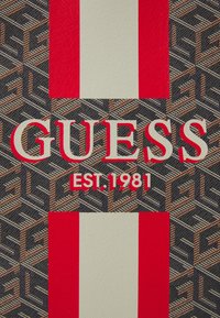 Wzorzysty materiał z czerwonymi i białymi paskami; na geometr backgroundzie przeplatających się kształtów wyraźnie widnieje napis "GUESS EST. 1981".