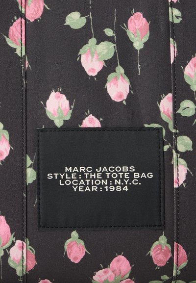 Черен плат с етикет, на който пише Marc Jacobs Tote Bag 1984, украсен с малки розови пъпки и зелени листа.