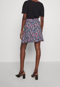 Jupe imprimée florale avec un fond bleu marine, ourlet volanté et taille ajustée. Associée à des talons noirs à bride arrière et un haut noir.