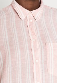 Camicetta button-up rosa chiaro con strisce verticali bianche, colletto a punta e taschino sul petto. Realizzata in un tessuto intrecciato e testurizzato.