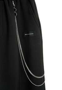 Joggers negros hechos de tela suave, con bolsillos laterales, una pequeña etiqueta y un detalle decorativo de cadena plateada.