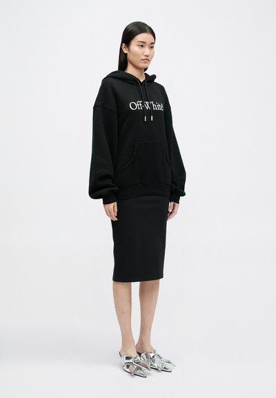 Černá mikina Off-White s bílým logem, oversized střih, přední kapsa; kombinováno s černou midi sukní a metalicky stříbrnými botami s špičatými akcenty.