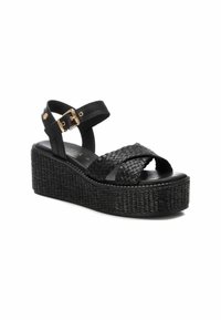 Sandalias de cuña negras con correas de cuero trenzado, hebilla ajustable en el tobillo, plataforma texturizada y plantilla suave. Presenta un acento de hardware dorado.