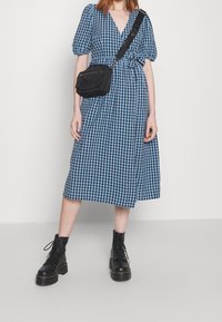 Blå och svart rutmönstrad klänning med puffärmar, åtsittande midja och full kjol, i kombination med svarta snörboots och en svart axelväska.