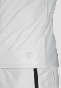 Weißes Sportshirt aus leichtem, glattem Material, mit einem dezenten grauen Logo und atmungsaktiven Netzpaneelen an den Seiten.