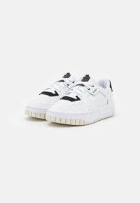 Vita sneakers med svarta detaljer och perforerad design. Har en tjock, texturerad sula och snören, med en liten grön logotyp på sidan.