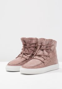Stivali alla caviglia in suede rosa con punta rotonda, lacci frontali, dettagli cuciti e suola in gomma bianca. Texture morbida e collo imbottito.