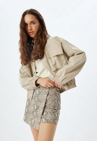 Beige oversized takki, jossa on elastiset hihansuut, yhdistettynä käärmeennahkakuosiseksi minihameeksi, jossa on teksturoitu muotoilu ja sivuhalkio.