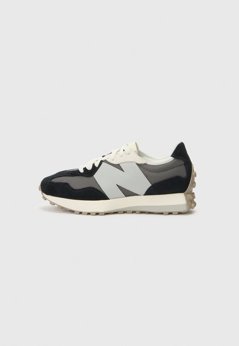 Baskets noires et grises avec des lacets blancs et un grand logo blanc "N" sur le côté, avec une semelle en caoutchouc beige à adhérence texturée.