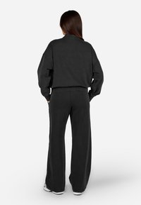 Čierny bavlnený sveter a široké nohavice v súprave, so voľným strihom, rebrovanými manžetami a hladkým povrchom, nosené s bielymi teniskami.